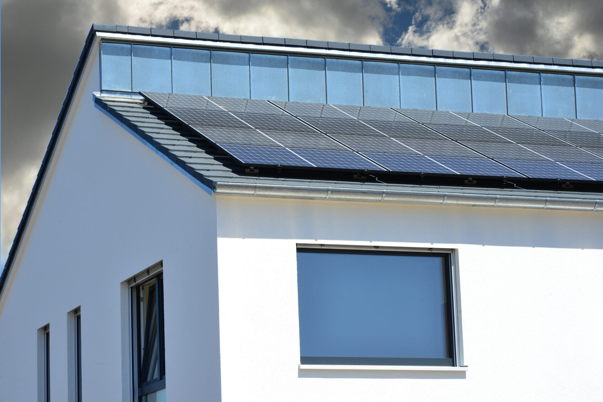 Modernes Einfamilienhaus mit Solaranlage auf dem Dach vor bewölktem Himmel; Sinnbild für erneuerbare Energien und umweltfreundliche Stromerzeugung im Eigenheim.