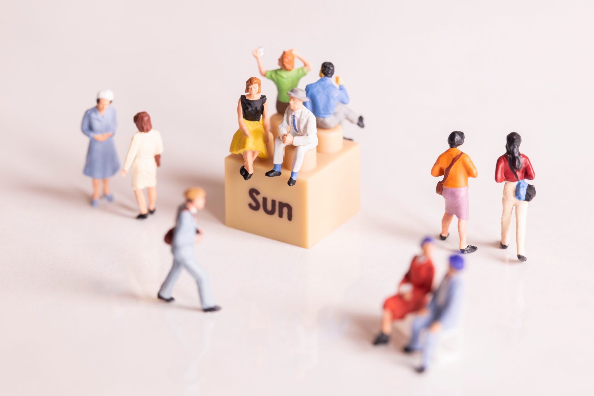 Mehrere Miniaturfiguren sitzen und stehen um einen Würfel mit der Aufschrift „Sun“; Symbolbild für sonnige Begegnungen und Gemeinschaft.
