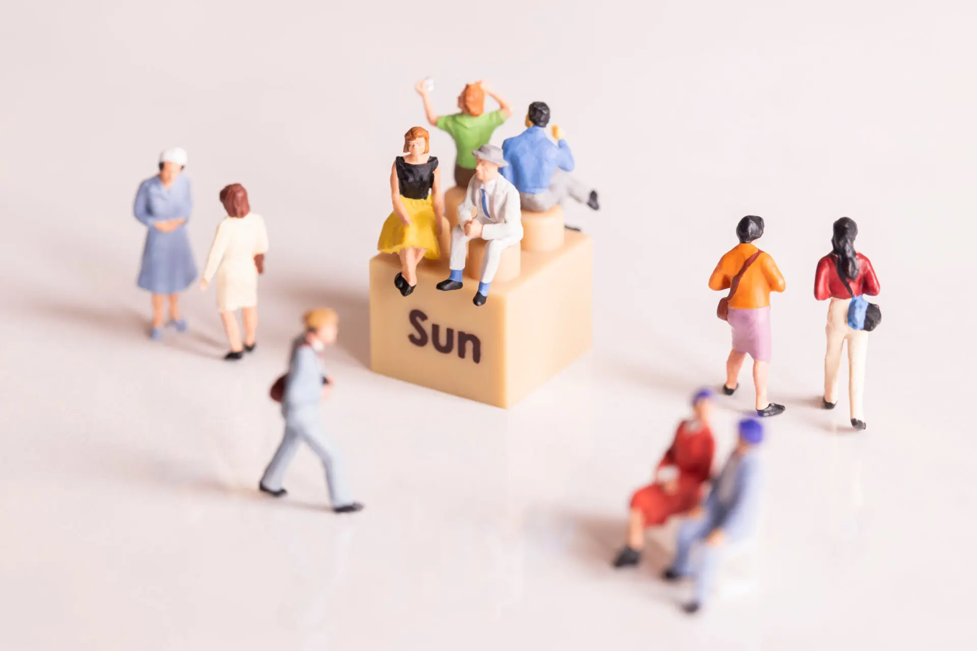 Mehrere Miniaturfiguren sitzen und stehen um einen Würfel mit der Aufschrift „Sun“; Symbolbild für sonnige Begegnungen und Gemeinschaft.
